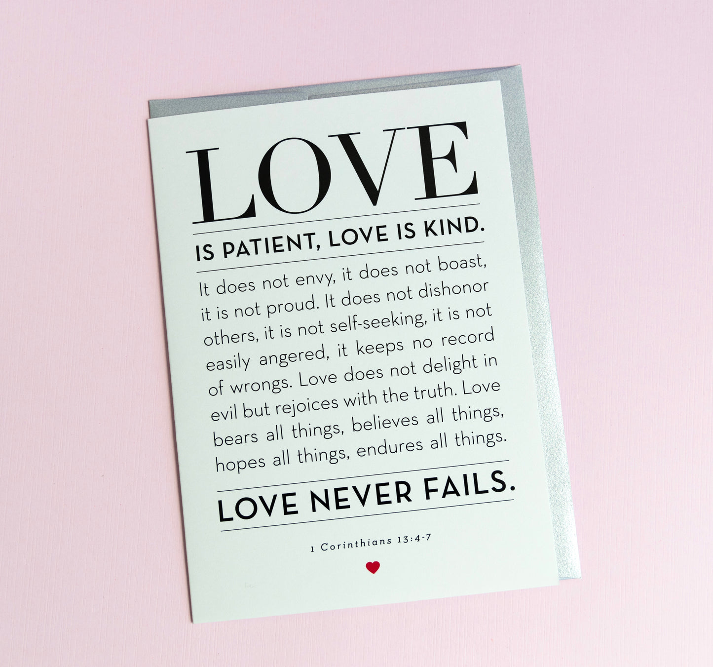 A greeting card with the words 'LOVE is Patient, Kind' from 1 Corinthians 13:4-7 printed on it, with a silver envelope. The card is blank inside and has a simple, elegant design.