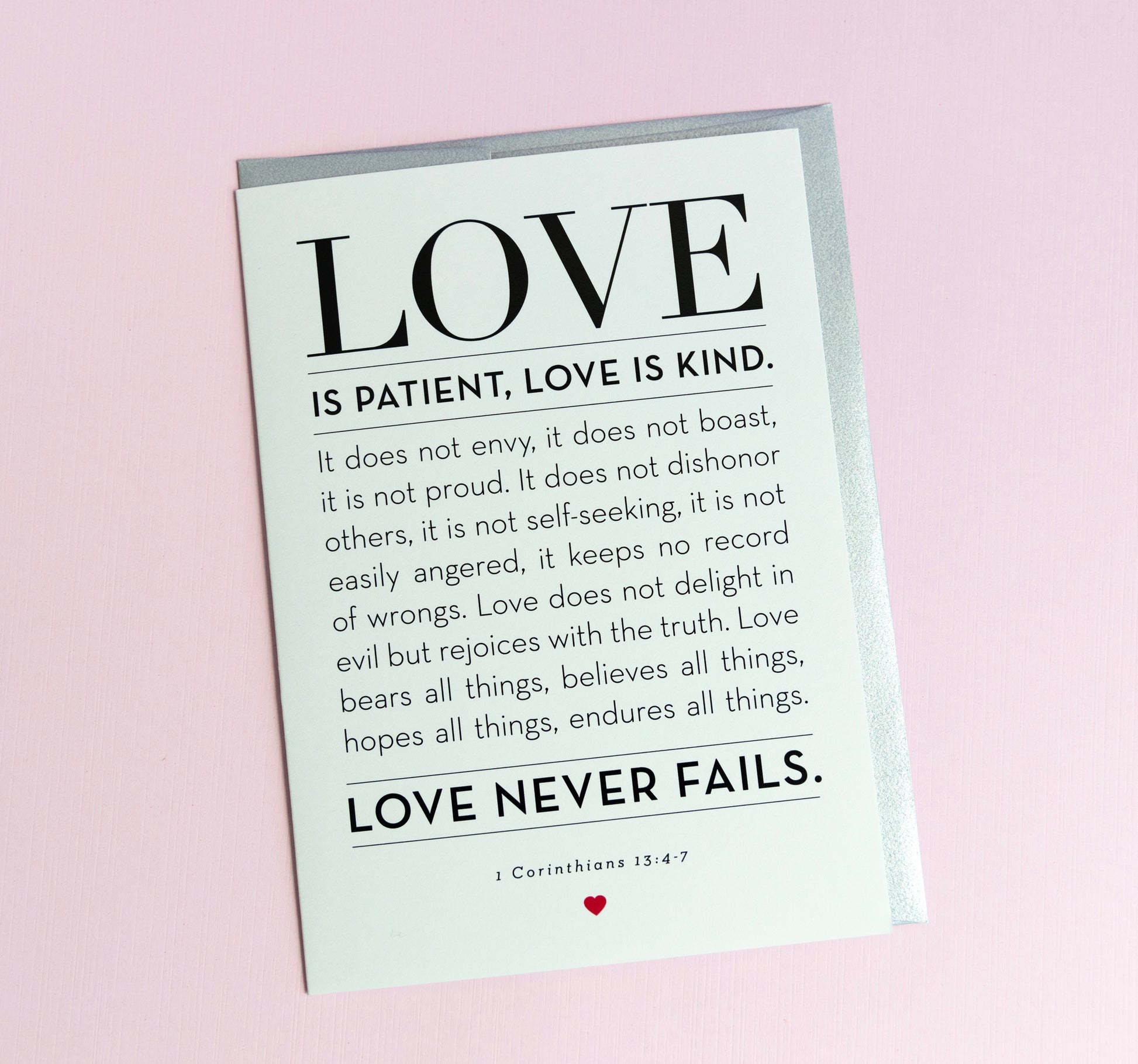 A greeting card with the words 'LOVE is Patient, Kind' from 1 Corinthians 13:4-7 printed on it, with a silver envelope. The card is blank inside and has a simple, elegant design.