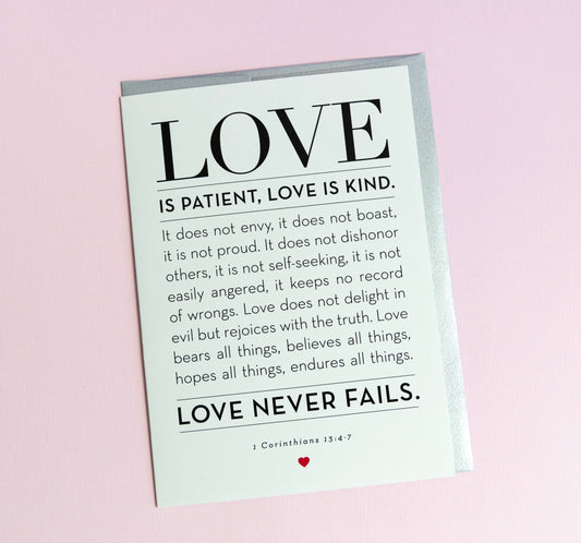 A greeting card with the words 'LOVE is Patient, Kind' from 1 Corinthians 13:4-7 printed on it, with a silver envelope. The card is blank inside and has a simple, elegant design.