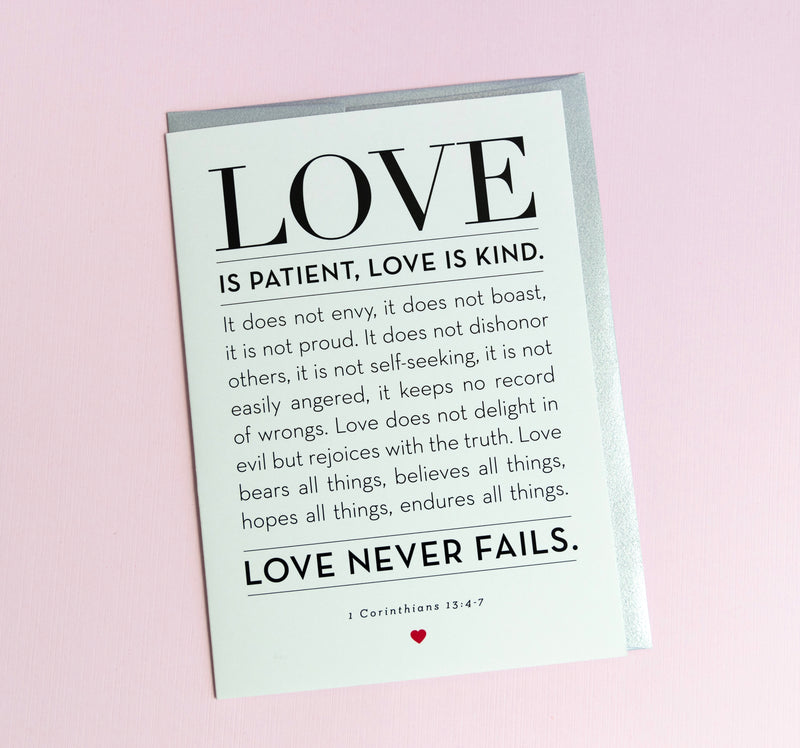 A greeting card with the words 'LOVE is Patient, Kind' from 1 Corinthians 13:4-7 printed on it, with a silver envelope. The card is blank inside and has a simple, elegant design.