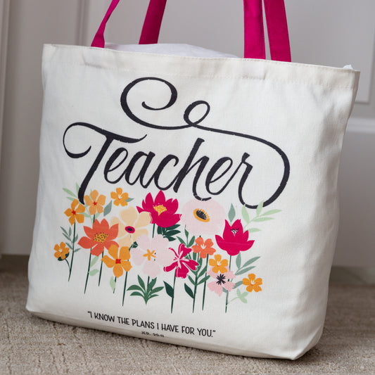 Tote bag with 'Teacher' text and floral design on a carpeted floor.